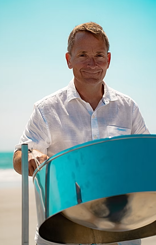 Professional picture of steel drum player for events playing blue colored drum at beachside event | Altus Entertainment