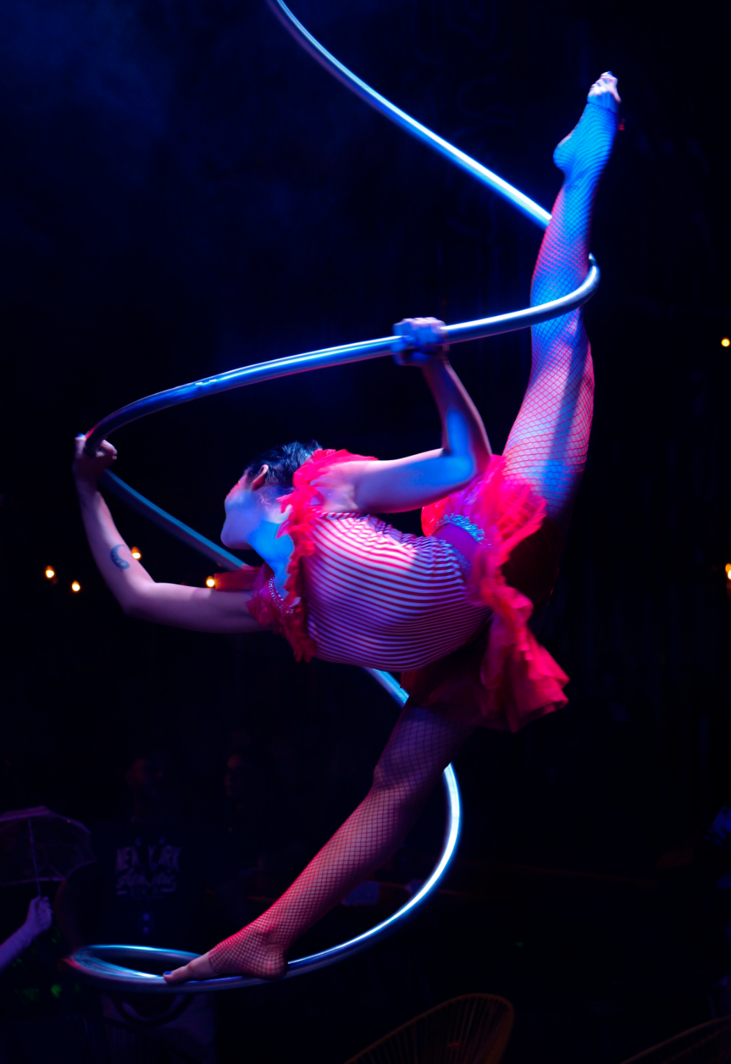 Female spiral aerial hoop artist wearing bright red colored costume and tights while twisting around aerial apparatus | Altus Entertainment